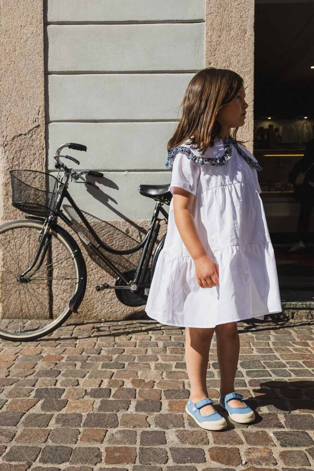 Abito Meringa Amtea indossato da una bambina accanto a una bicicletta appoggiata al muro