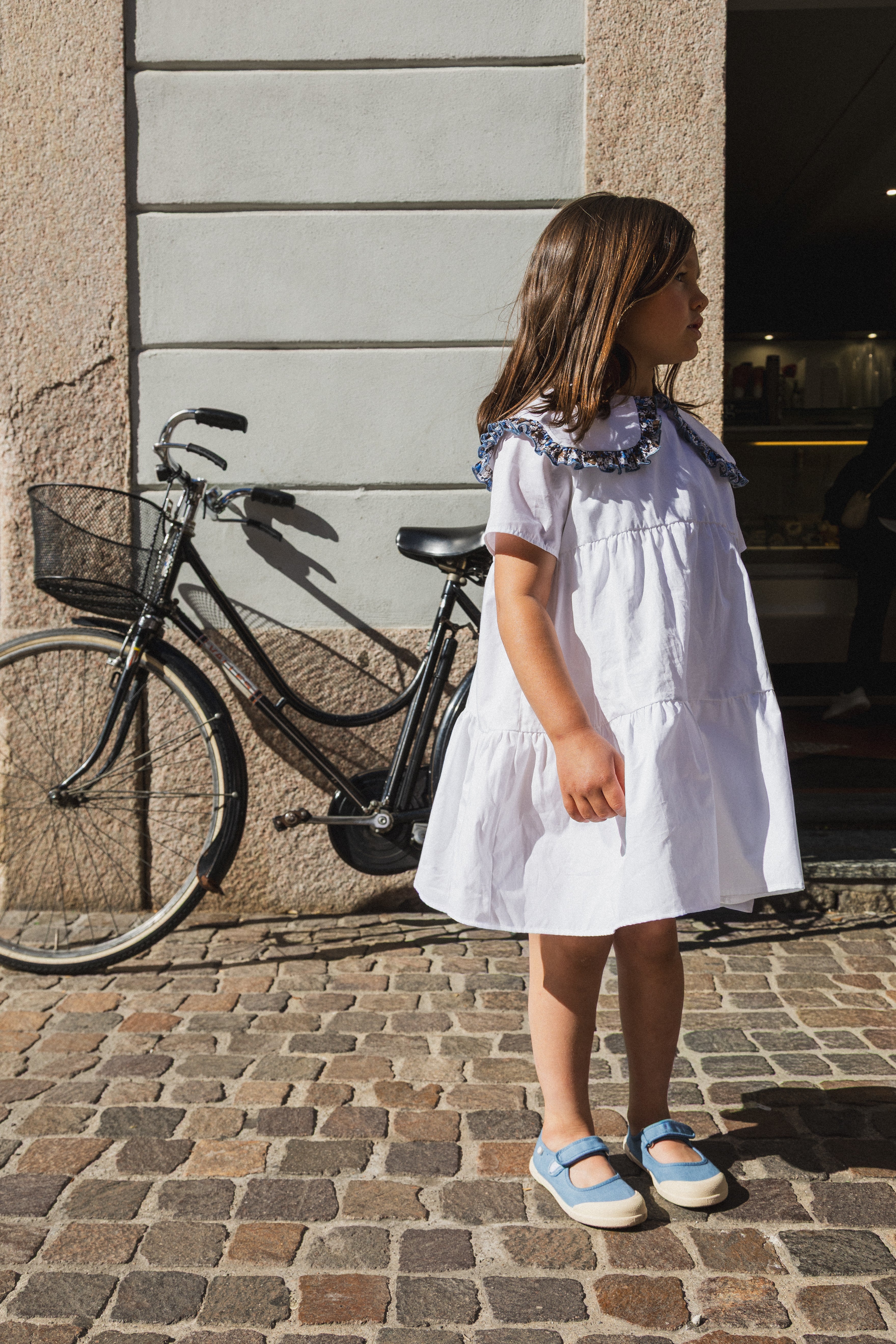 Abito Meringa Amtea indossato da una bambina accanto a una bicicletta appoggiata al muro
